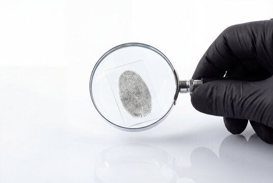 Hand in black glove holding magnifying glass over fingerprint for investigation