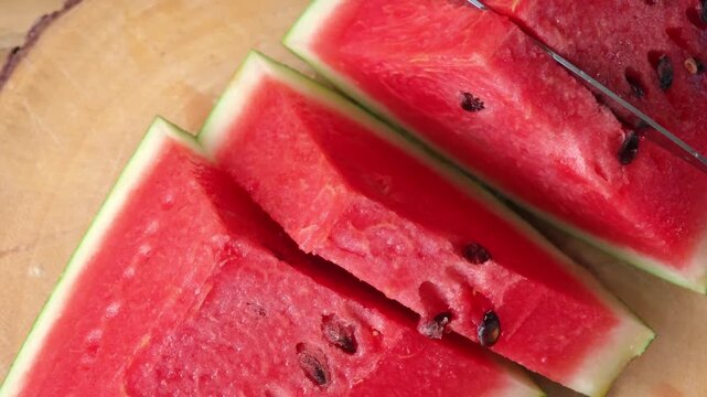 Female hands cutting fresh juicy watermelon slices on cutting board.