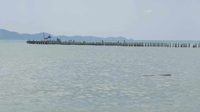Concrete piles standing in calm water near the pier with overcast sky and distant shoreline visible in the background