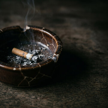 Ashtray with smoking cigarette and ashes on wooden surface  