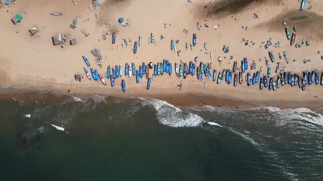Aerial top view of fishing boats lined on sandy beach with waves in Kovalam Kerala India