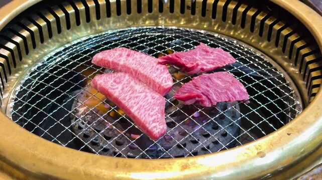 Raw premium wagyu beef slices cooking on Japanese charcoal grill net with tongues moving meat.