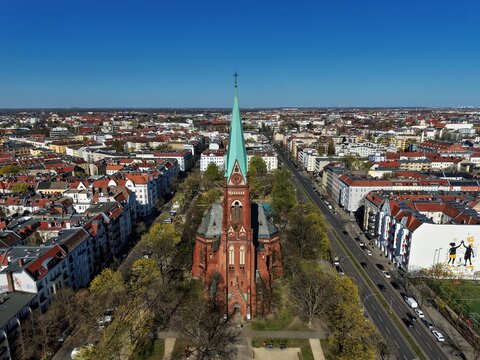 Aerial view of the historic Nazareth Church at Leopoldplatz surrounded by green trees and urban residential buildings under a clear blue sky in Berlin, Berlin, Germany.