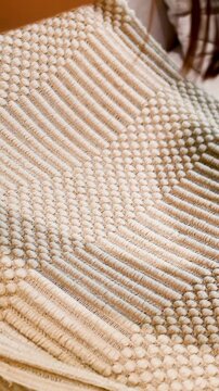 Person Spreading a Beige Woven Textured Rug on a White Sofa