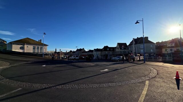 Street curves past houses and parked van under low sun at Port-en-Bessin, Normandy, France