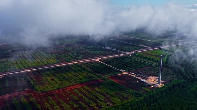 Low clouds hanging above a wind turbine site with structured land below. Aerial view captures the boundary between cloud layer and renewable energy infrastructure across the landscape.