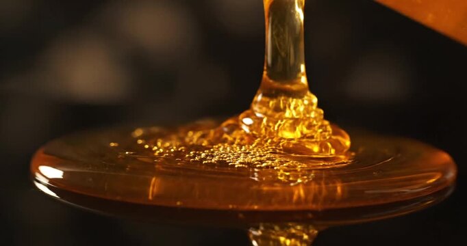 Golden honey pouring from a spoon onto a reflective surface, showcasing its viscous texture