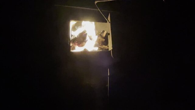 Close-up of bright orange flames flickering inside a traditional metal stove in a Kyrgyz yurt at night, creating a warm and cozy atmosphere during a remote mountain expedition