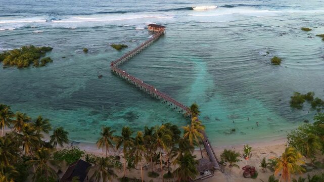 Panoramic aerial view of General Luna coastline at sunset, Siargao. Drone shot of the lush palm tree forest, Cloud 9 boardwalk, and the glowing horizon over the Philippine archipelago.