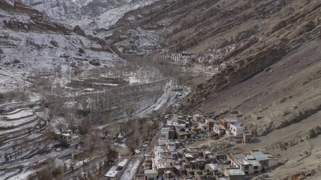 Hemis Monastery and village occupy a steep Himalayan gorge in Ladakh, India, surrounded by snow-dusted ridges and sparse winter vegetation. Smooth lateral tracking shot reveals remote village.