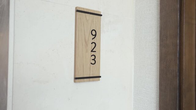 Cinematic push-in shot focusing on a minimalist wooden room number sign in a luxury boutique hotel. Elegant interior design highlighting premium architectural materials, 
with braille signage