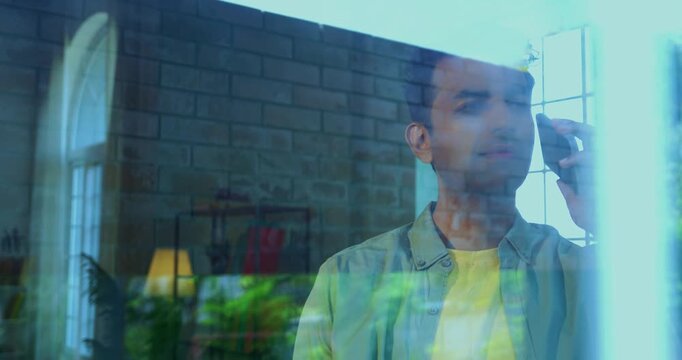 Indian impatient young man dialed phone using smartphone and waiting for someone to pick standing near glass window in modern Indian home with view from outside showing reflections on glass
