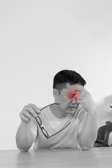 Asian man with eye pain holding glasses in monochrome portrait with red pain highlight