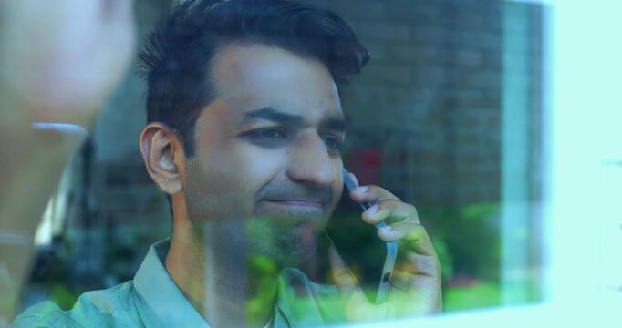 Indian impatient young man distressed because routine call fail using smartphone standing near glass window in modern Indian home with view from outside showing reflections on the glass pane