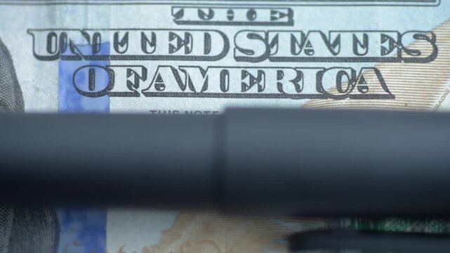 Closeup US note under ultraviolet inspection showing shifting illumination across United States of America lettering, security ribbon and ink details, paper texture and microprint