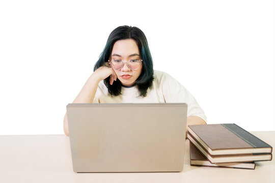 Bored or Tired Young Woman Student Looking at Laptop Screen with Books on Desk