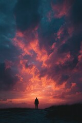 Obraz premium Silhouette of person standing under dramatic sunset sky