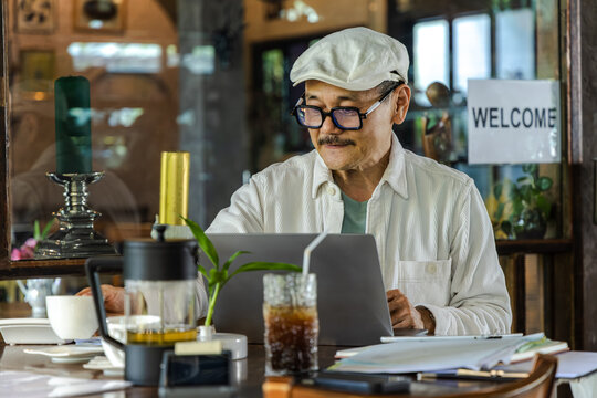 Senior Cafe small business entrepreneur reviewing documents beside laptop digital workflow managing finance and accounting tasks modern management technology improving efficiency and organization