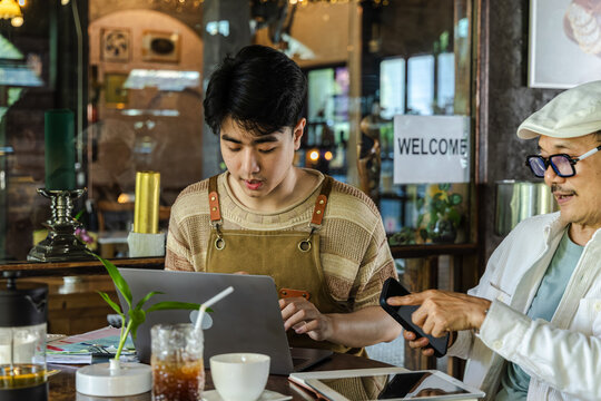 Modern family small business digital management, senior cafe owner guiding young barista worker or son sharing experience teamwork learning growth trust technology management lifestyle in coffee shop
