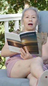 Vertical video: Reading senior woman reacting to offscreen sound on porch with ENDLESS SUNSETS book
