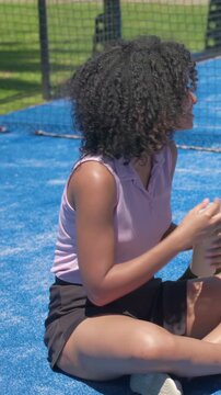 Vertical video: Smiling woman in pink polo opening bottle on blue court hearing voice, hydrating