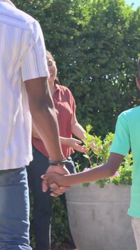 Vertical video: Approaching mother, dad in jeans and son inspecting pink planter on patio, greeting