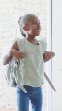 Vertical video: Door opening youth wearing green top and jeans entering foyer, adjusting backpack
