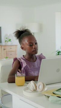 Vertical video: Typing child in purple dress at table, mother approaching, guiding with laptop