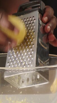 Vertical video: Zesting lemon as hands angling grater over bowl in kitchen catching zest for dish
