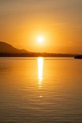 Naklejka premium Panoramic view of a peaceful ocean at dawn during golden hour with bright sun and hazy hills in the distance