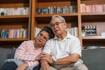 Fototapeta premium Elderly couple sits closely on a couch. Happy elderly couple playing video games at home, concept of active retirement lifestyle and technology in aging.