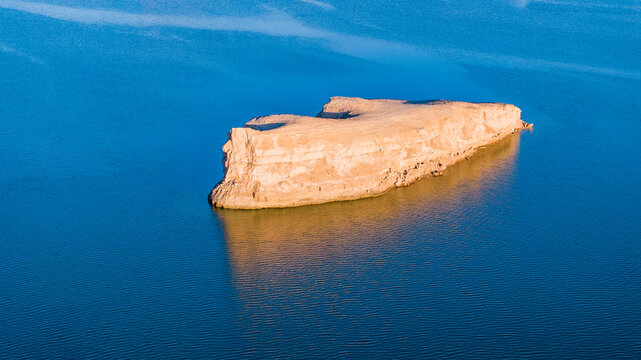 Aerial view of Yadan landforms rising from turquoise water in Dachaidan, Qinghai, China. Unique desert geology forming island-like rock formations in a rare water-covered Yardang (Yadan) landscape.