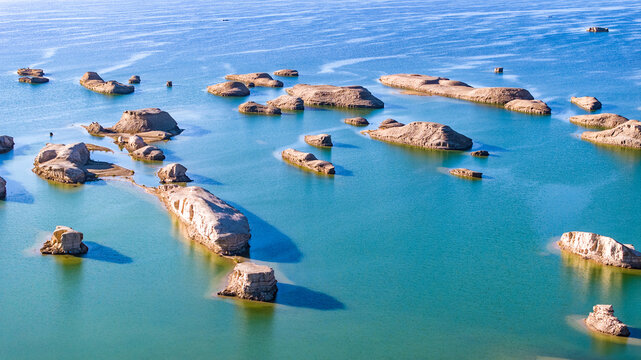 Aerial view of Yadan landforms rising from turquoise water in Dachaidan, Qinghai, China. Unique desert geology forming island-like rock formations in a rare water-covered Yardang (Yadan) landscape.