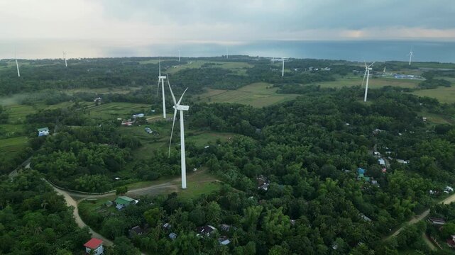 Aerial view of wind turbines over lush tropical greenery with an ocean horizon in Guimaras, Visayas, Philippines&mdash;renewable energy infrastructure in a coastal rural environment.