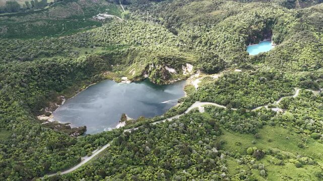 Clockwise drone orbit over geothermal lakes in Waimangu Volcanic Valley, New Zealand, stunning forest trees and volcanic landscape.