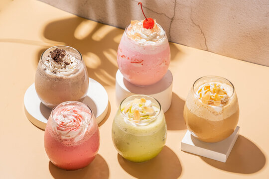 lady paraula ice drink esmeralda cream, prince of sahara, sanset in thaif, and love in aden. served on a white coaster in a clear glass cup, with a brown base and a gray background 