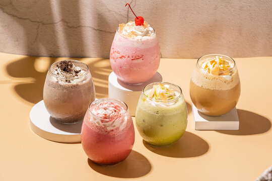 lady paraula ice drink esmeralda cream, prince of sahara, sanset in thaif, and love in aden. served on a white coaster in a clear glass cup, with a brown base and a gray background 