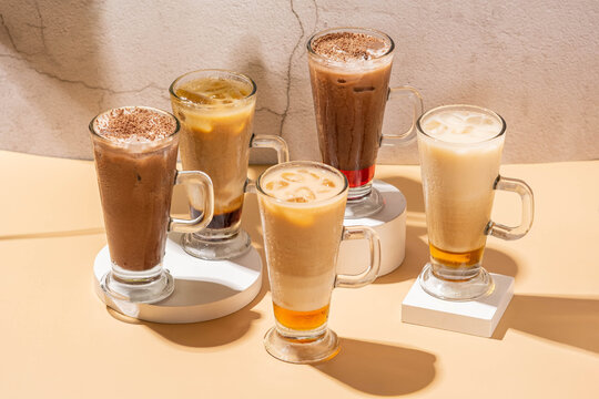 Caramel late ice, choco bery, original chocolate, hazelnut late, and brown sugar served in clear glass and on a white coaster with a brown base and a gray background 