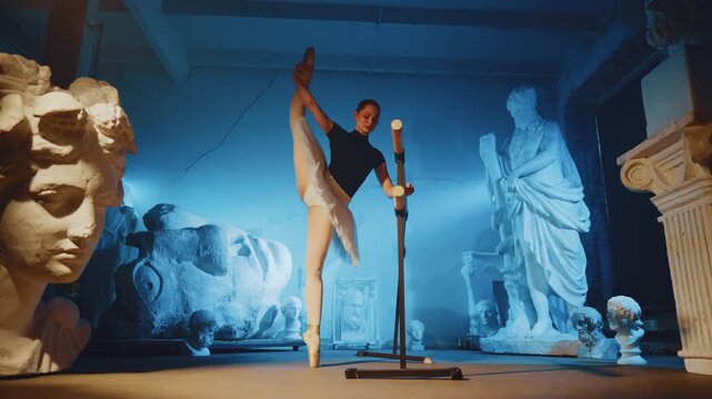 Flexible ballerina rehearsing and training in studio, standing near ballet barre . Dark hall of museum of classical arts, contemporary ballet dance performance, choreography and music for inspiration