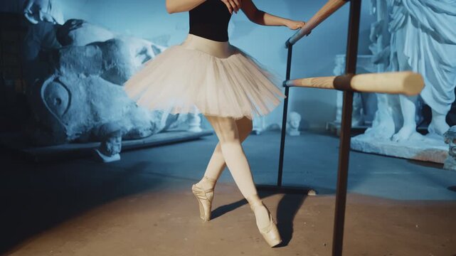Ballerina near barre, woman dancing in rehearsal class, details view on legs. Slender lady performing classical choreography, training for stay prima in theatre, classical art and music, female beauty