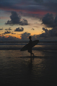 Surfer silhouette wading through sea under vivid sunset sky, Bali