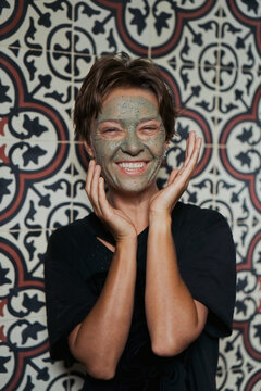 Laughing woman with green clay face mask in Balinese bathroom