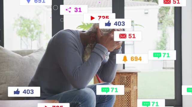 Mature man checking red phone on sofa by glass doors, social alerts multiplying, layering over him