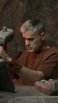 Prehistoric accountant sitting at his desk, he is using a calculator and carving a financial report on a stone tablet using a hammer and a chisel