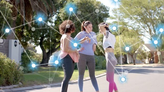 Three women checking fitness watch on street, activating node overlay linking them and high-fiving
