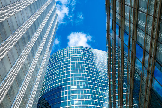 Expansive modern architecture scene of glass office skyscraper building facade reflection in Paris France with clustered towers upward perspective blue sky depth and scale