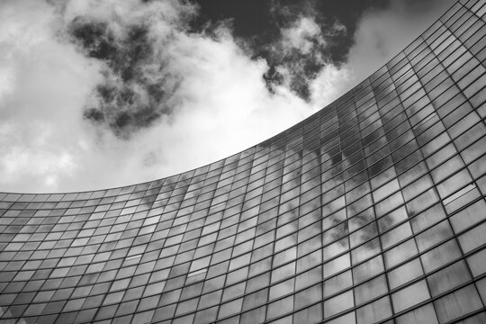 Monochrome view of modern architecture where glass office skyscraper building facade reflects sky in Paris France with curved lines dramatic contrast and grid pattern