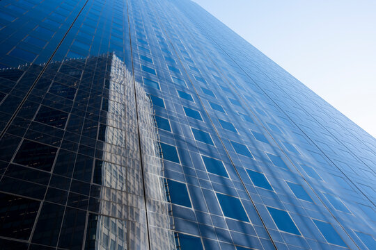 Upward perspective on modern architecture as glass office skyscraper building facade reflection stretches in Paris France with minimal sky sleek height and vertical grid lines