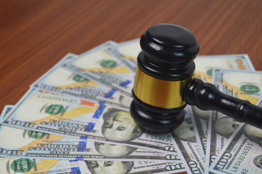 Gavel of justice and legal authority rests on scattered dollar bills, symbolizing financial power, court settlements, and economic law
