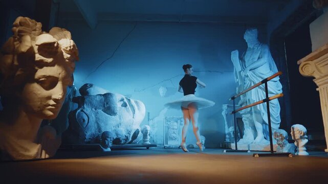 Woman in tutu dancing classical ballet choreography in dark studio in night. Pretty young ballerina rehearsing alone in room with ancient statues of Greek gods, contemporary art performance in museum